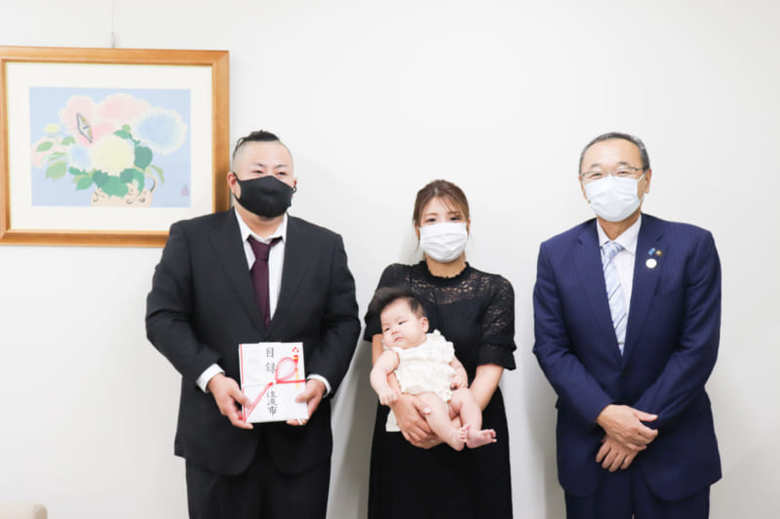 「多子世帯出産成長祝金事業」の第１号として、渡辺竜五佐渡市長（右）から目録が贈られた伊藤さん一家