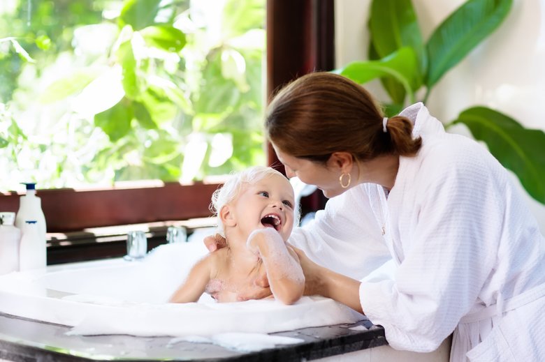 Mother washing baby in bubble bath. Water fun.