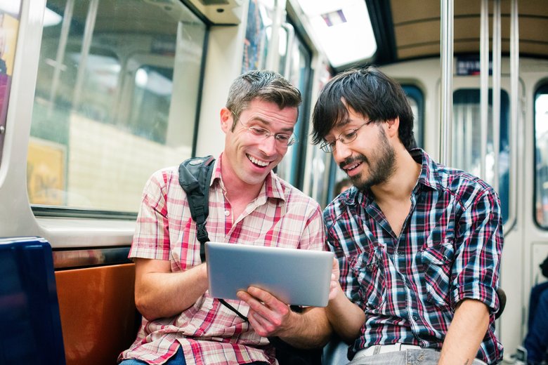 Two male commuters in subway laughing at tablet