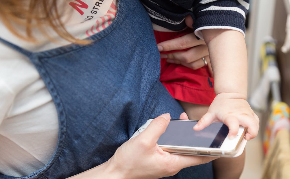子どもを抱っこしてスマホを触るママ