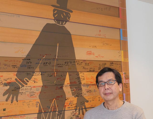 子供達の成長を刻んだボードの前に立つ西田さん