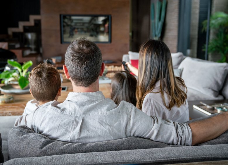 Backview of family at home watching TV while mom changes channels