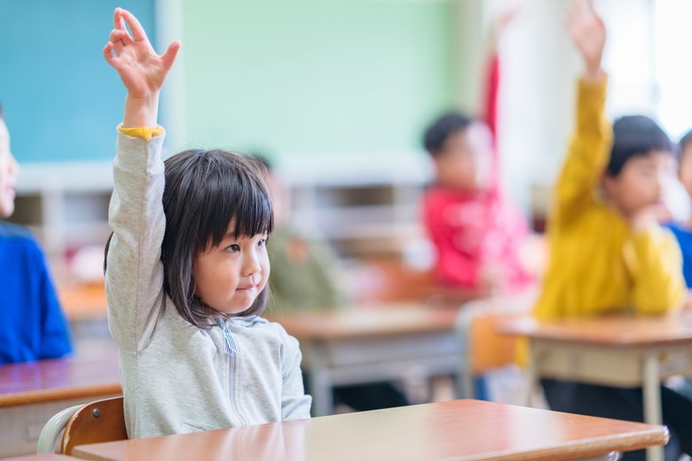 Cute elementary school girl raising hand in classroom