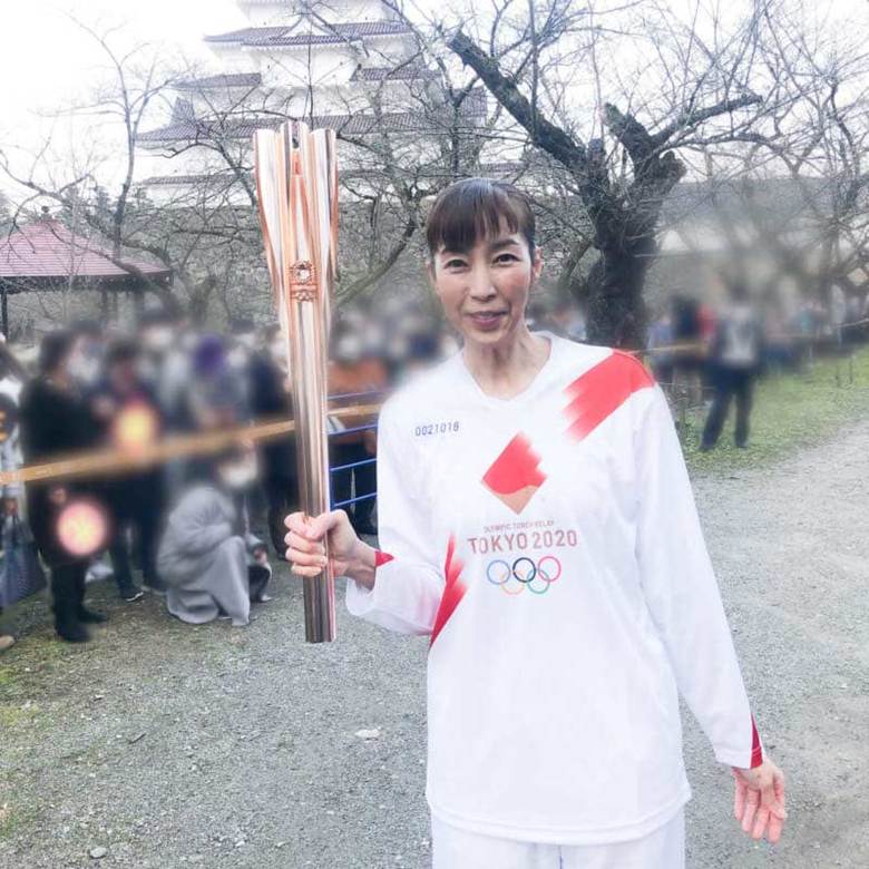 鶴ヶ城をバックにトーチを掲げる大林さん（プライバシー配慮のため一部修正）