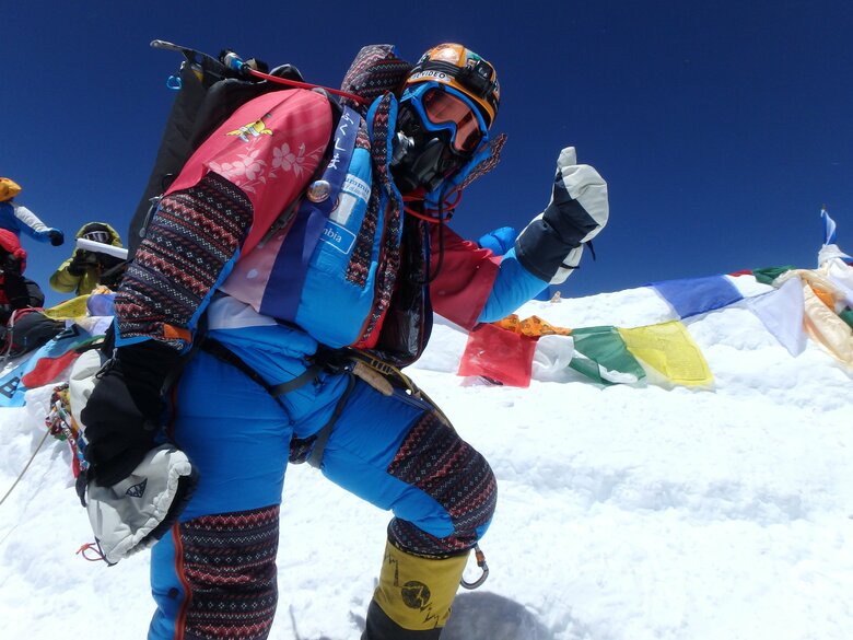 エベレスト登山中のなすびさん　後ろにはチベット仏教の祈りの旗タルチョが並ぶ