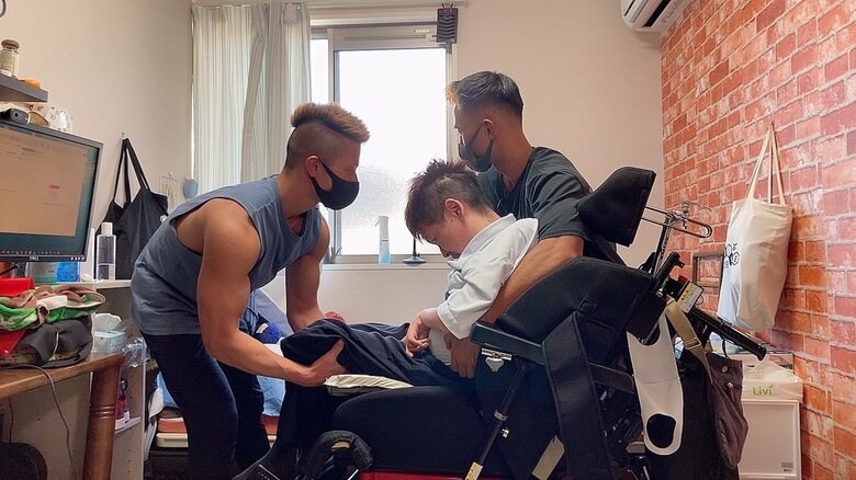 利用者の方の体を抱える際に腕の筋肉が目立つ吉村さん（写真右）