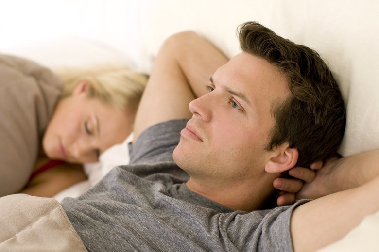 Man in bed with hands behind head next to a sleeping woman