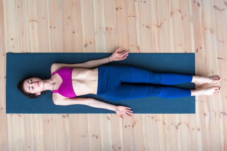 Top view of young woman lying in corpse or dead body pose relaxing after practicing yoga