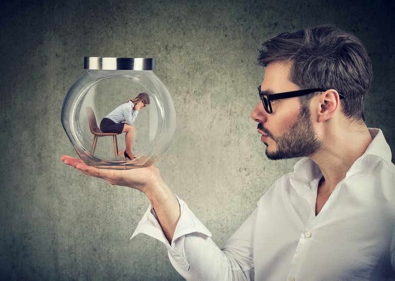 Business man holding a glass jar with a young sad business woman trapped in it