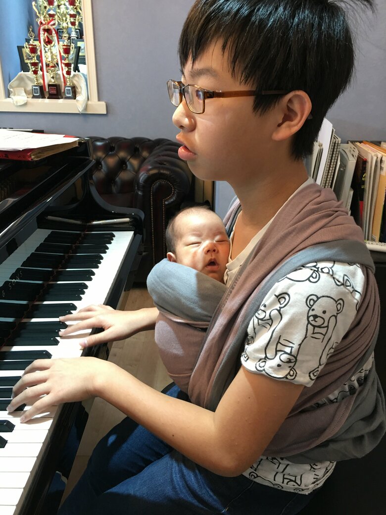 14歳下の妹さんを抱っこしながらピアノを弾く中学2年生の順一朗さん