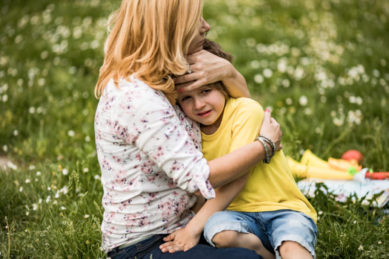 Mother consoling her crying son at the park.