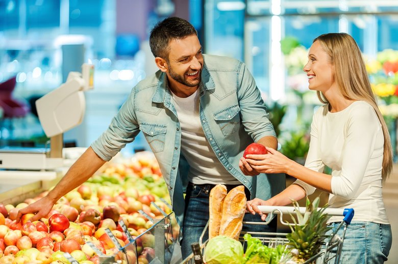 Beautiful young smiling couple choosing apples in supermarket together