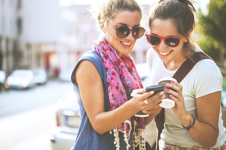 Happy female friends reading a text message outdoors