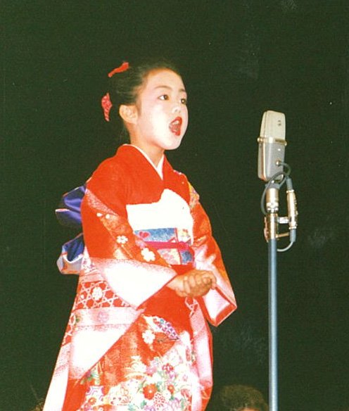 着物を着てステージで民謡を歌う幼少期の丘さん