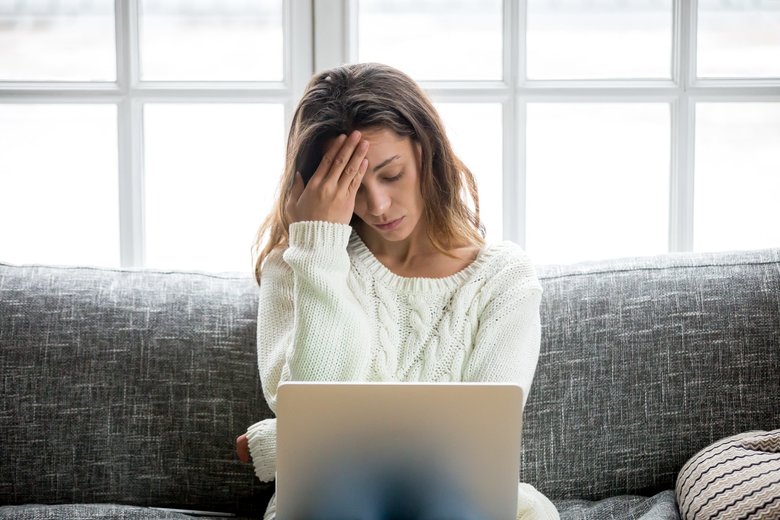 Frustrated woman worried about problem sitting on sofa with laptop