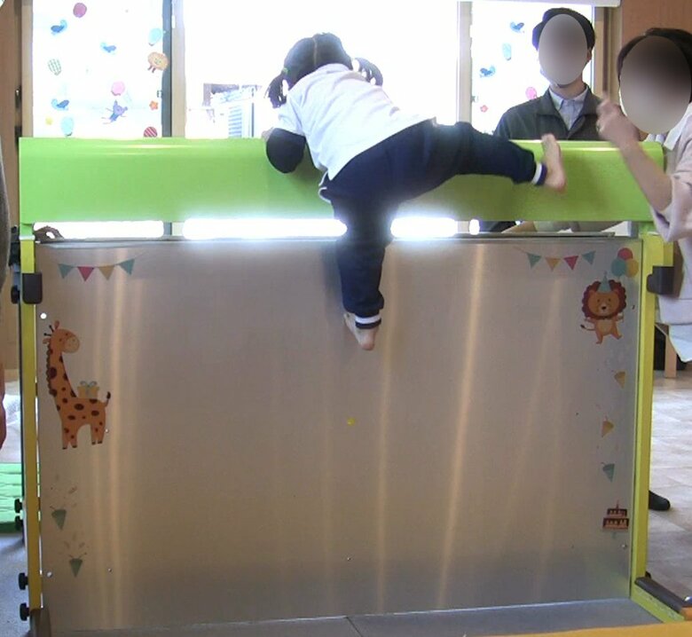 ベランダの柵に見立てた120cmの高さの実験機を登る4歳の子ども。壁の上部に手を引っ掛けながら、足も使って器用に乗り越えている