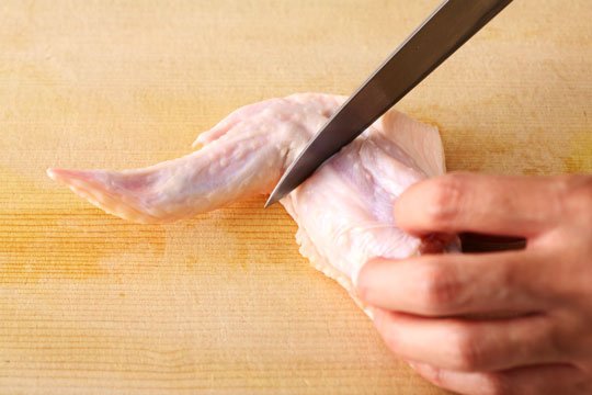 【チューリップを作る】手羽先は関節の位置が見えやすいように、皮面を下にしてまな板におく。関節から1㎝ほど下のところ(手羽中側)に切り込みを入れる。切り込みは骨に当たるまで入れ、骨に対して直角に切り込みが入るようする。