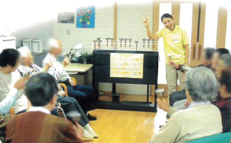 ハンドベルを使って利用者と触れ合う当時の高橋さん／画像提供：（株）ハートライフケア デイサービス ゆらり