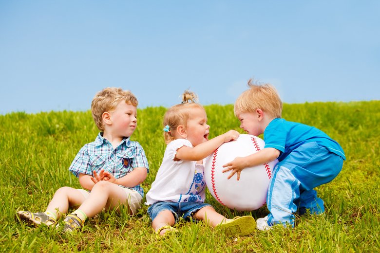 Three toddlers playing with large ball outside in the grass