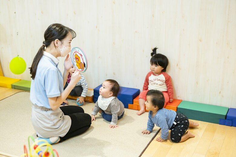 0歳児のクラスを担当する村山さんと、動物のイラストが登場する遊びに夢中の子どもたち