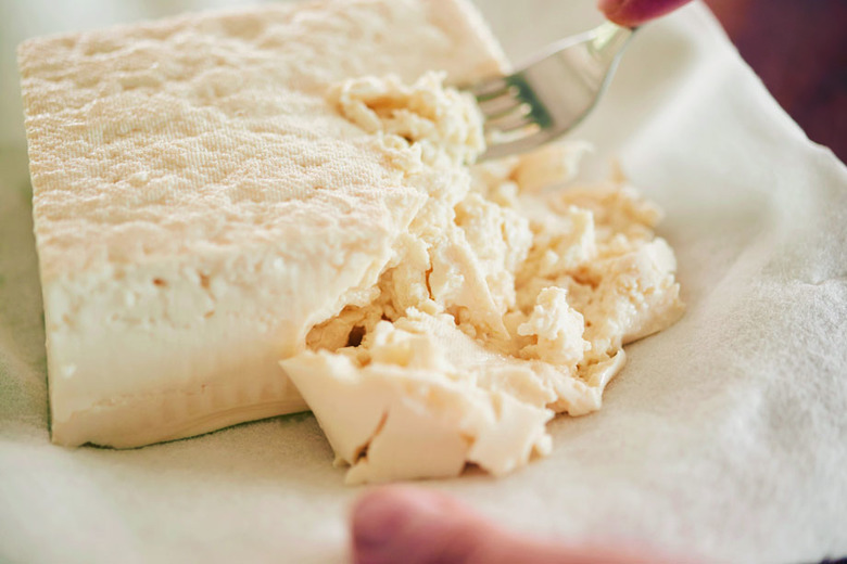 耐熱皿にキッチンペーパーを敷き、豆腐をのせる。フォークなどで粗くつぶし、キッチンペーパーをのせて上から押さえる。電子レンジ(600W)にかけて4分加熱する。