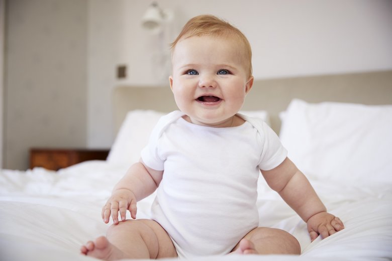 Happy Baby Boy Sitting On Parents Bed