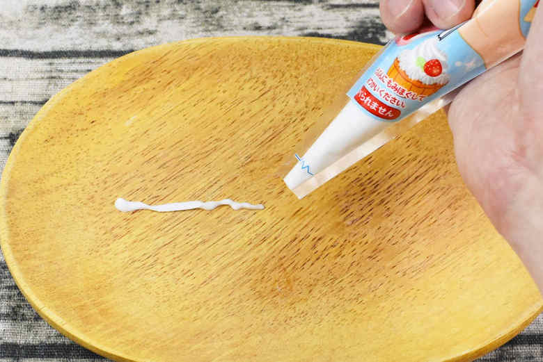 角にプリントされた点線に沿って、パッケージの角を直線にカット。この状態でパッケージをグッと掴み、強めに握ると、カットした口から白い粘土がにゅるっとお目見え。粘土は水気が多く、かなり柔らかい印象です。直線に切ったので、口からはチューブ状の白い粘土がどんどん出てきます。黒い紙の上で使えば、粘土で絵が描けそうですね。