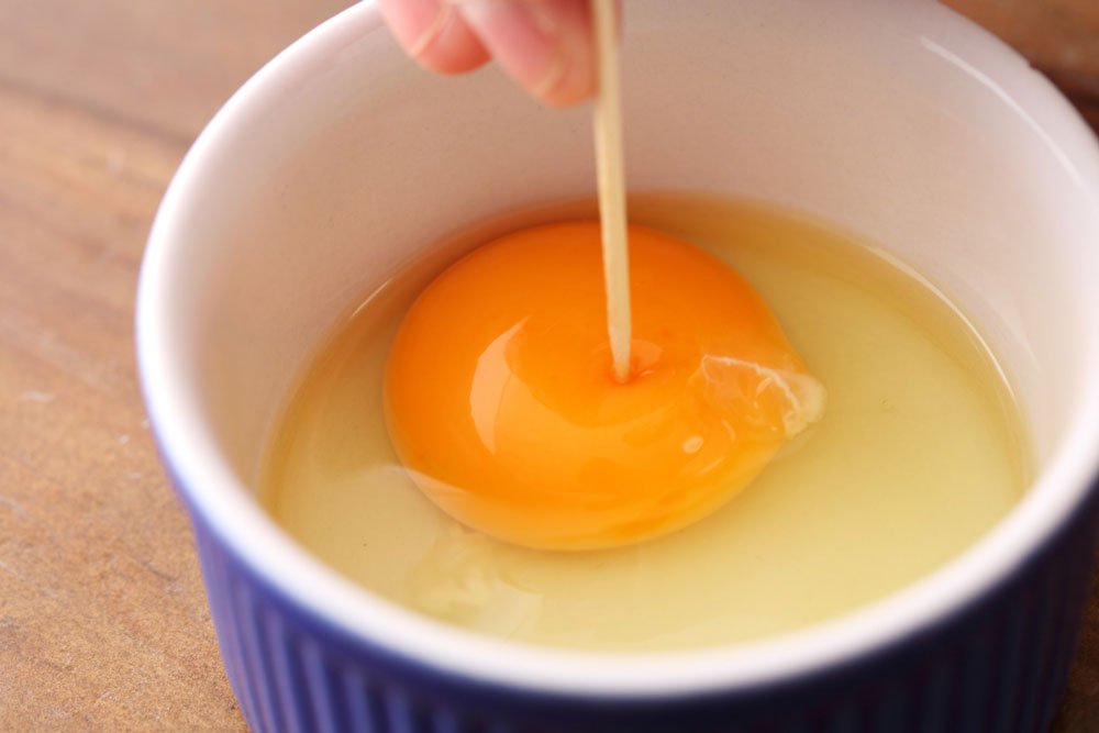 生卵の黄身に爪楊枝で穴を開けるところ