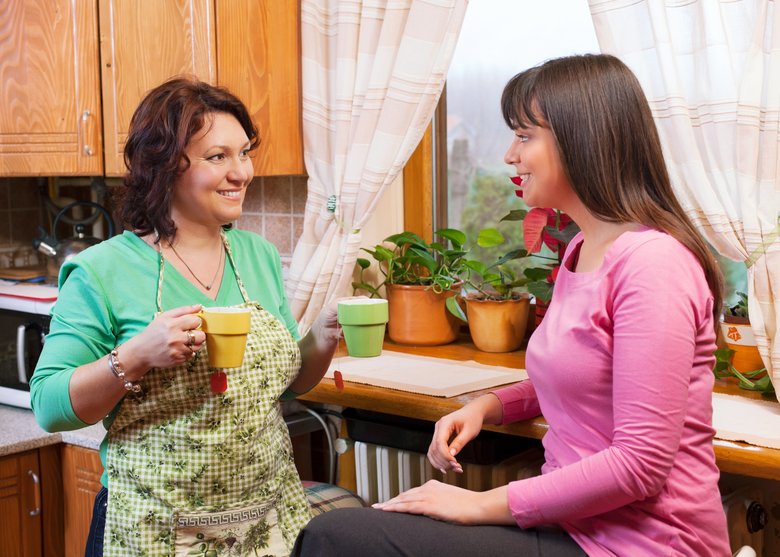 Mother and daughter talking, drinking tea in kitchen