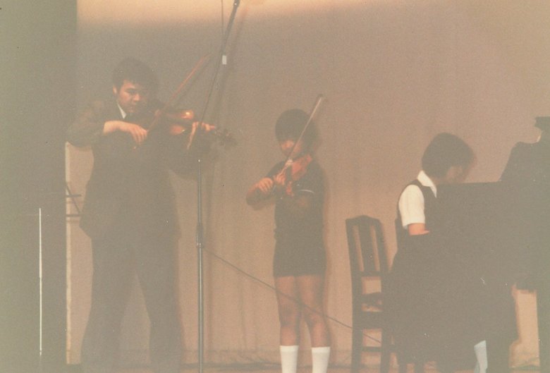 弟（中央）の発表会でバイオリンを演奏する父（左）とピアノを弾く中学1年生当時の高橋さん（右）