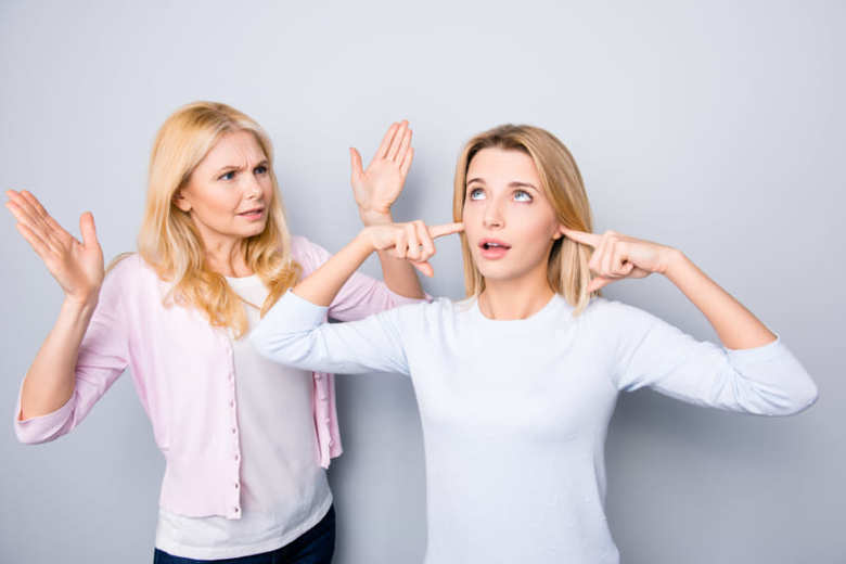 Carefree daughter close ears with index fingers ignoring arguments of her nervous stressed angry mother gesturing with hands bring up upbringing concept isolated on grey background