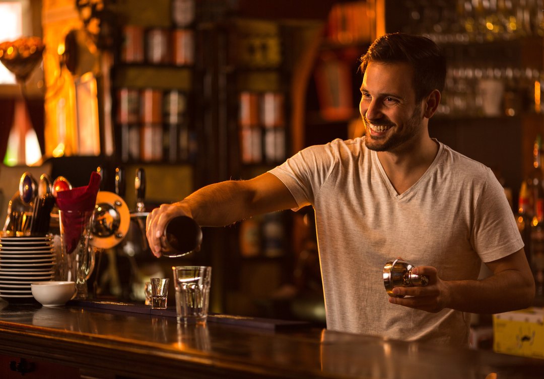 Happy bartender at bar counter preparing a cocktail.