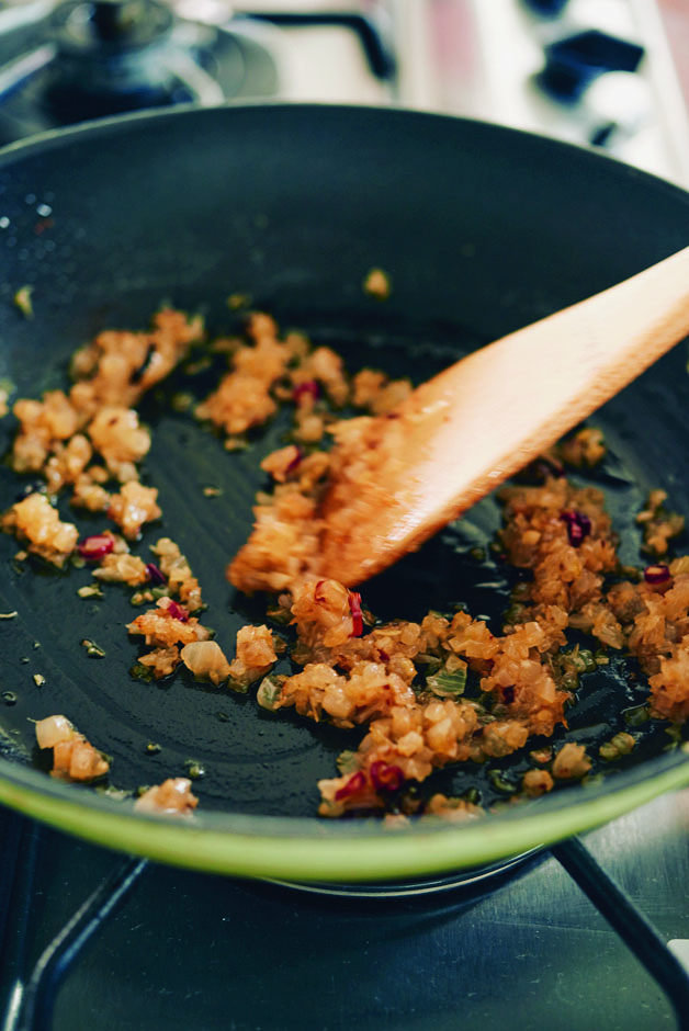 フライパンにサラダ油、赤唐辛子を入れて火にかけ、玉ねぎを中火で炒める。色づくまで7～10分炒めたら、にんにく、しょうが、トマトを加える。トマトの形がくずれてペースト状になるまでさらに炒める。