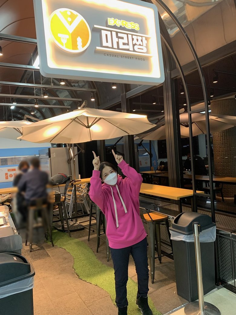 韓国語の看板の前でポーズをとる関根さん