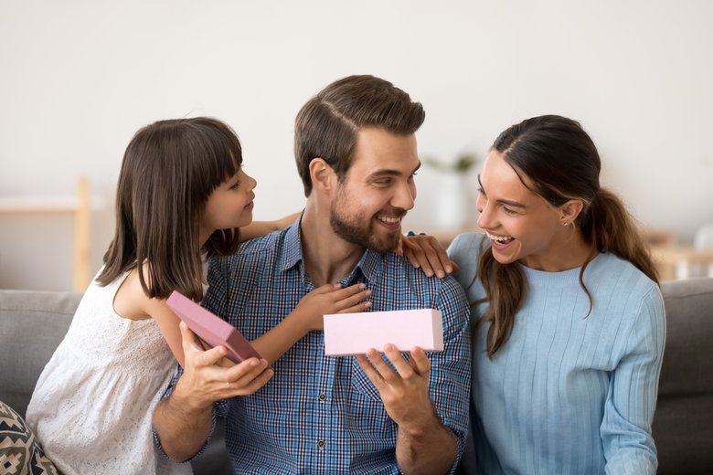 Cute daughter and wife congratulating happy father opening gift box