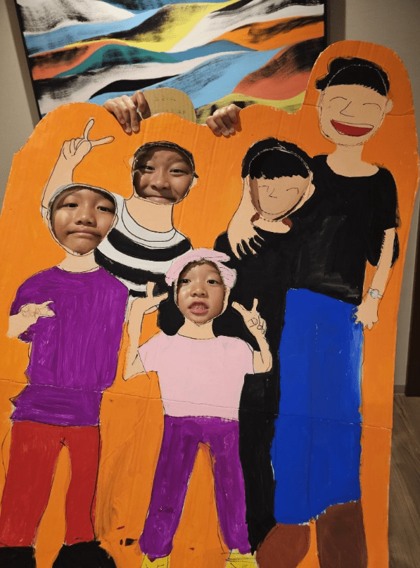 次男せいはち君が制作した家族作品に顔はめする（左から次男せいはち君、長男せいきち君、長女こうめちゃん）