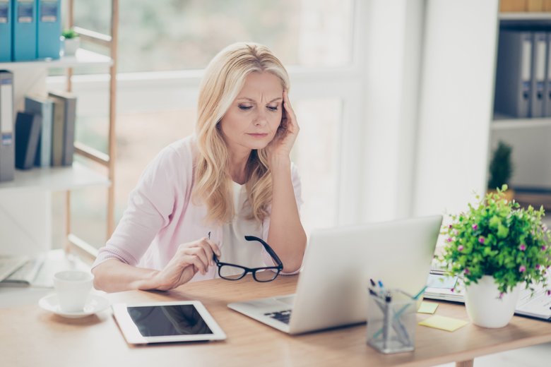 Upset, unhappy, pretty, charming, professional teacher feeling bad, took off glasses, touching her temple, suffering from headache, sitting at desk in workstation, having computer, tablet on the table