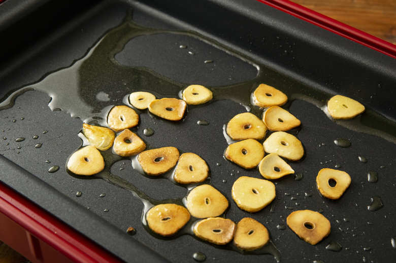 ホットプレートにオリーブオイルとにんにくを入れて低温にし、焦がさないように気をつけながらにんにくの両面をこんがり焼く。きれいな狐色になったら一度にんにくだけ取り出す。