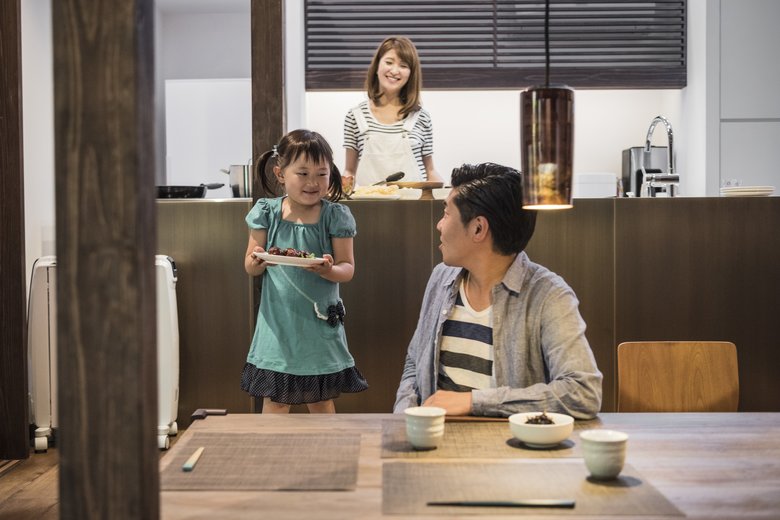 Young Japanese girl carrying food to father at table