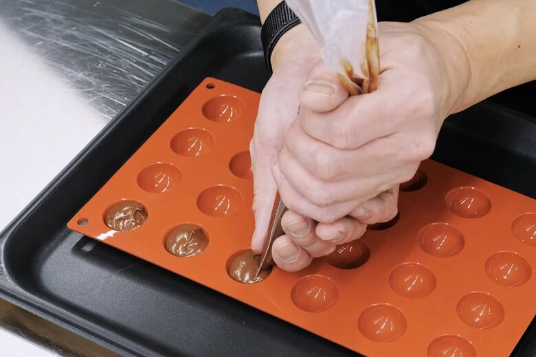 【作り方14】絞り袋に生地を詰めて型に絞り込んでいく。型の代わりに、鉄板いっぱいにチョコソースを広げて、冷凍室で固まったらひと口サイズにカットするのもOK