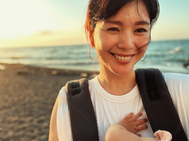 抱っこ紐で娘と自宅近くの海辺の散歩をする知花さん。夕陽と海を背景に爽やかな笑顔！