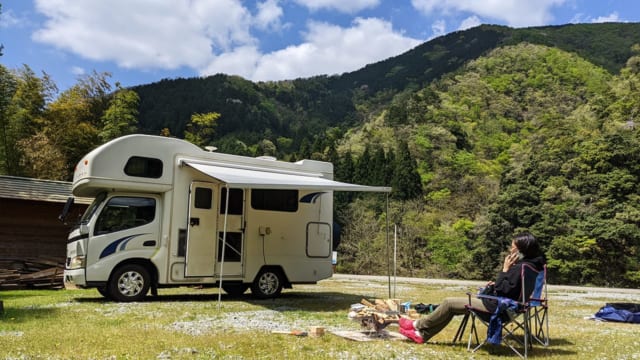 雄大な自然のもと、愛車の前で電話をするむっちゃん