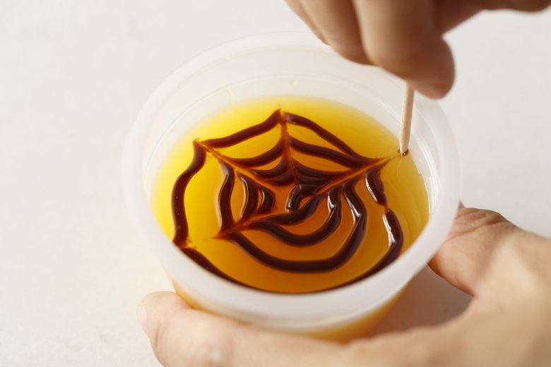 パンに塗るチョコクリームをポリ袋に入れ、よくもみながら袋の隅に寄せる。先端を少し切って絞り口にすして、ゼリーの表面にうずまきを描く。さらに下写真のように、つまようじで中央から外に向かって放射状に線を引く。線を1本引くたびにつまようじをふくと、きれいに仕上がりますよ
チョコはもみながら体温で少しやわらかくしておくと作業しやすい