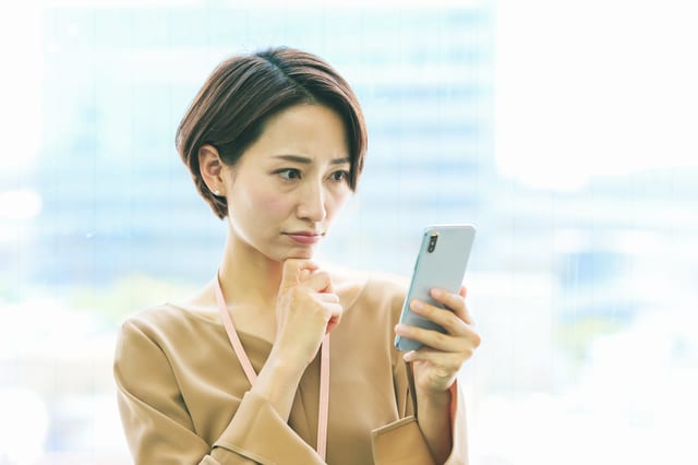 スマホを見ながら悩む女性