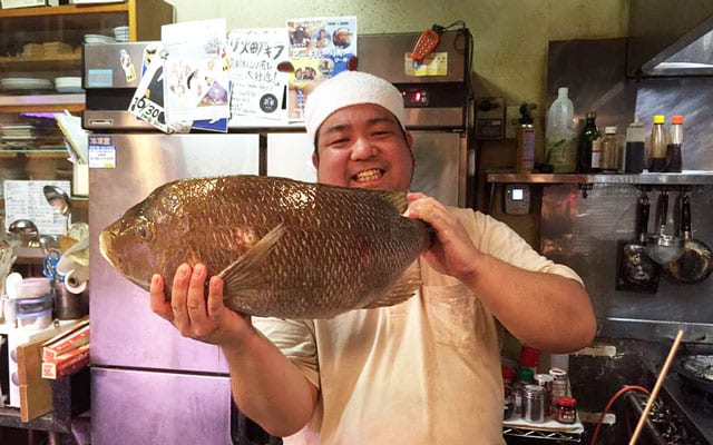 店に立ち魚を持つ竹内さん