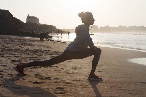 ジョギングの前に浜辺でストレッチをする女性の画像
