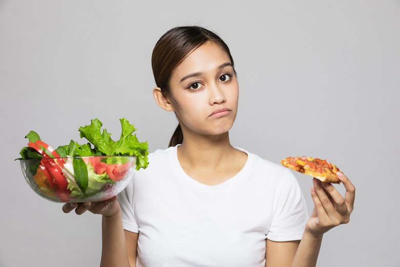 Young woman holding salad bowl and pizza.